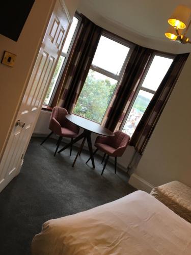 um quarto com uma secretária e 2 cadeiras em frente às janelas em Coniston Guest House em Sheffield