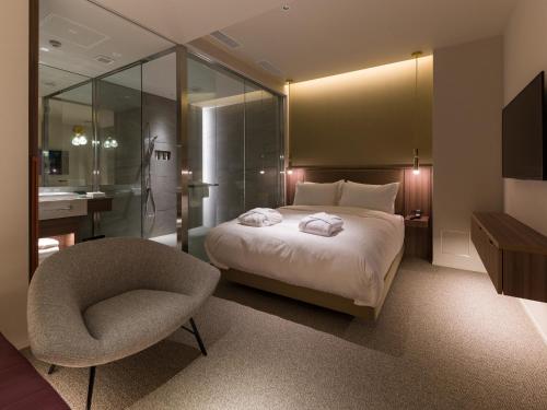 a bedroom with a bed and a chair and a bathroom at THE skM TOKYO HOTEL & DINING in Tokyo