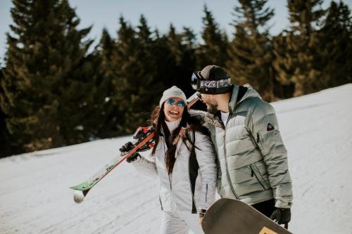 a man and a woman walking in the snow with a snowboard at Apart & Spa Zoned in Kopaonik