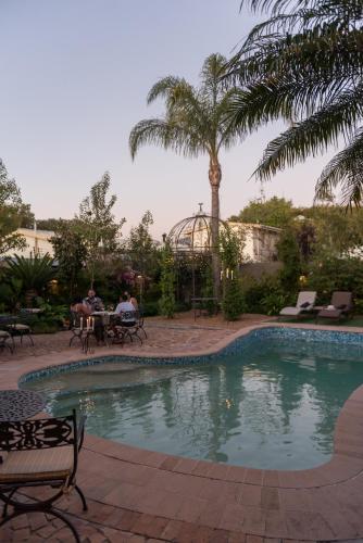 a swimming pool with palm trees and people sitting at a table at Baruch Guesthouse on Lovell in Stellenbosch