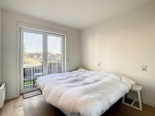 a white bedroom with a large bed and a large window at Appartement 'Witte Berg' De Panne in De Panne
