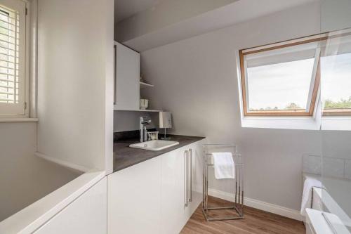 uma cozinha branca com um lavatório e uma janela em Cosy Home Near Sunningdale/Ascot/Wentworth Golf Club em Sunninghill
