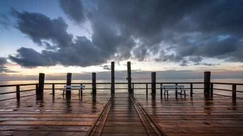 zwei Bänke auf einem Pier mit wolkigem Himmel in der Unterkunft Lütt Nest Föhr in Alkersum