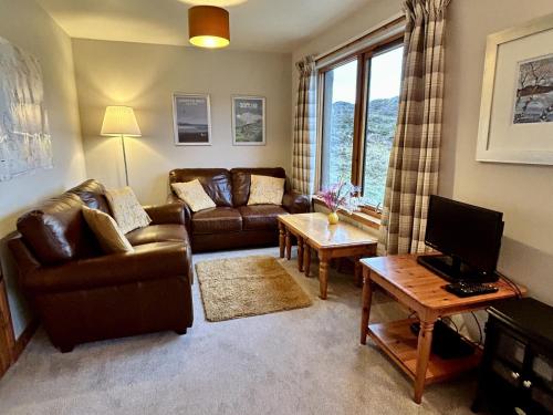 a living room with couches and a table and a television at Myrtle Cottage in Lairg