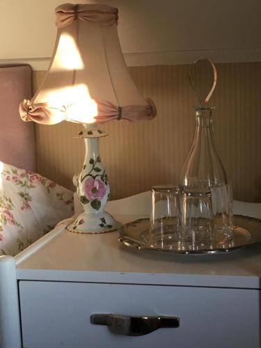 una mesa con una lámpara y dos vasos. en Handlarens villa - Vandrarhem de luxe en Söderbärke