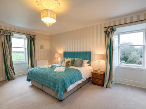 a bedroom with a bed and two windows and a chandelier at Vicarsford Farmhouse with Hot Tub in Leuchars