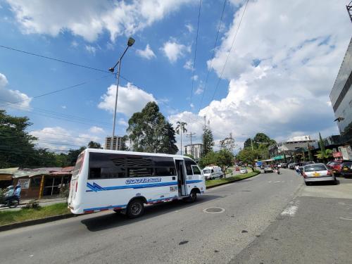 a white bus is driving down a city street at APARTAESTUDIO en el Norte de Armenia, en la via a Salento y Filandia Con parqueadero de carro in Armenia