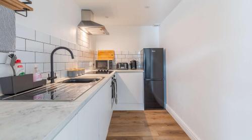 een keuken met witte werkbladen en een zwarte koelkast bij Brand New Central Balcony Flat - Hastings Holidays in Hastings