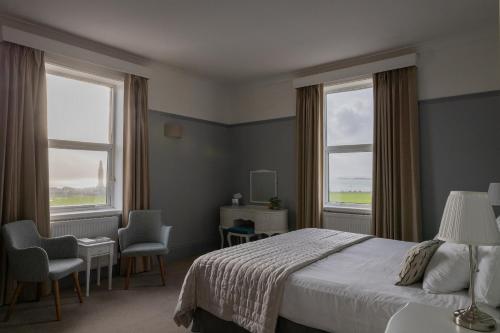 a bedroom with a bed and two chairs and two windows at The Queens Hotel in Portsmouth
