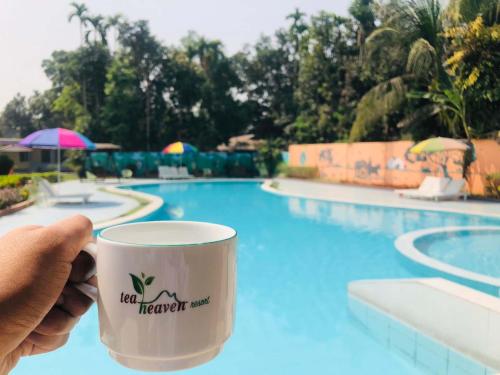 a person holding a coffee cup in front of a pool at Tea Heaven Resort in Sreemangal