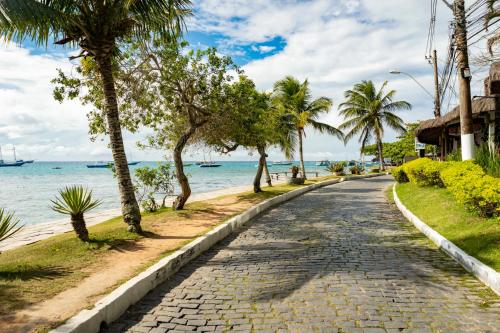 a cobblestone street next to the ocean with palm trees at Suri Búzios Hotel in Búzios