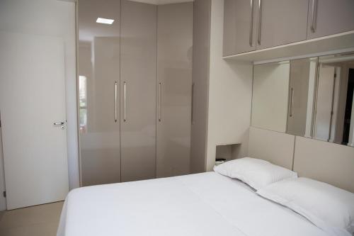 um quarto com uma cama branca e armários brancos em Apto moderno próximo à Praia de Itaparica ES em Vila Velha