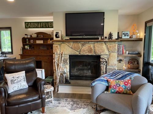 a living room with a fireplace with a tv and chairs at Mountain Condo with Modern Cabin Style in East Jewett