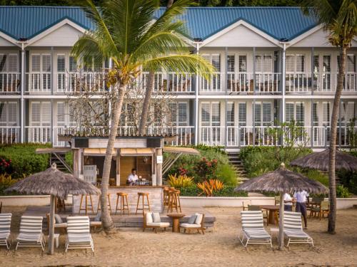 a hotel on the beach with chairs and tables and palm trees at Soho Beach House Canouan in Canouan