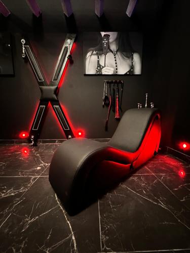 Habitación negra y roja con silla negra con luces rojas en Loveroom de luxe - Thème 50 nuances de grey maison privative spa insolite, en Douchy-les-Mines