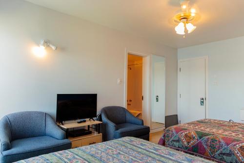 Pokój z 2 łóżkami i 2 krzesłami oraz telewizorem w obiekcie Auberge de la Rivière Saguenay w mieście La Baie