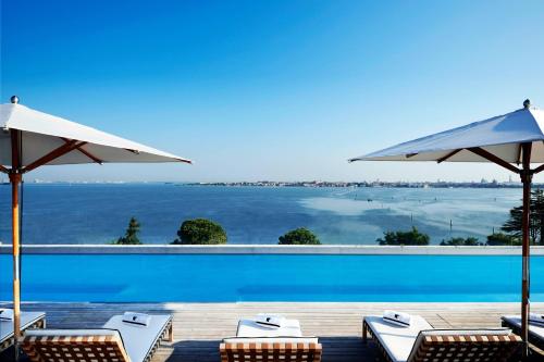 a pool with chairs and umbrellas and the ocean at JW Marriott Venice Resort & Spa in Venice