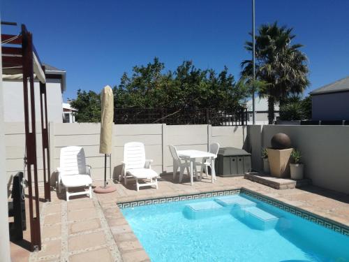 uma piscina com cadeiras brancas e uma mesa e uma mesa e cadeiras em Captain's Sea Cabin em Cidade do Cabo