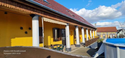 um edifício amarelo com colunas brancas ao lado de uma piscina em Panzio A mi Paradicsomunk em Véménd