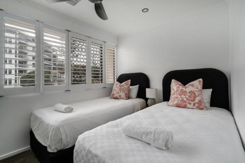 two beds in a bedroom with white walls and windows at Nimolanca - 3 Bedroom Partial Ocean View in Caloundra