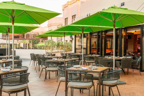 a restaurant with tables and chairs with green umbrellas at Le Méridien Dubai Hotel & Conference Centre in Dubai