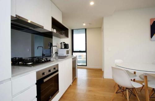 cocina con armarios blancos, mesa y encimera en Bright Bundoora Apartments, en Melbourne