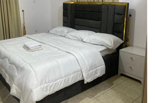 a large white bed with a black headboard and white pillows at Beautiful 2Br Apt in Ogba, Ikeja, Lagos in Lagos