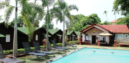 a resort with a swimming pool with chairs and a house at Tranquility Cottage Resorts in Baga
