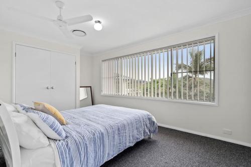 a white bedroom with a bed and a window at The Wreck Room Holiday House close to the Beach with Ample Boat Parking in Shoal Bay
