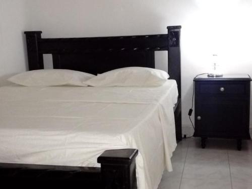 1 cama con sábanas y almohadas blancas y mesita de noche en Room in House - Taminaka Hostel en Santa Marta - Shared room 3, en Santa Marta