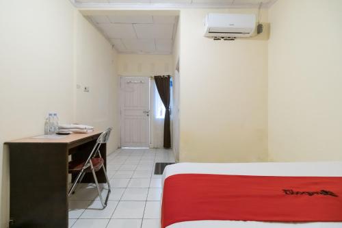 Habitación con cama y escritorio con manta roja. en RedDoorz Syariah At Jalan Raflesia Nusa Indah Bengkulu, en Bengkulu