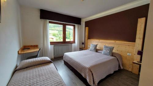 a bedroom with two beds and a desk and a window at Hotel Angelo in Comano Terme