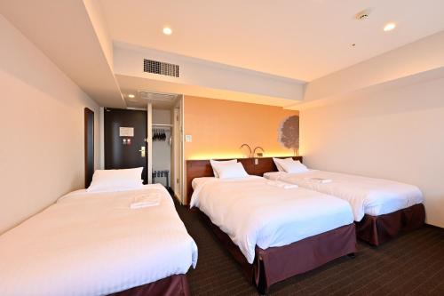 two beds in a hotel room with white sheets at Hotel Keihan Sapporo in Sapporo