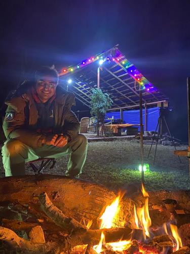 a man sitting in front of a fire at night at Dreamwoods A travellers farm in Dharamshala