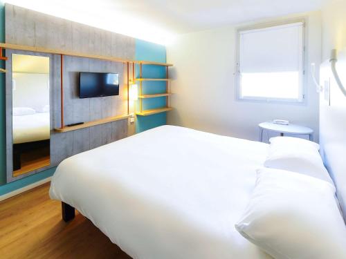 - une chambre avec un grand lit blanc et une télévision dans l'établissement Ibis budget Dijon Centre Clemenceau, à Dijon