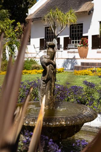 a fountain in front of a house with flowers at Cape Village Lodge in Durbanville