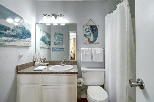 een badkamer met een wastafel, een toilet en een spiegel bij Beach Club Seas the Day in Padre Island