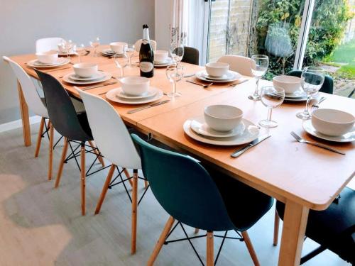a wooden table with chairs and plates and wine glasses at Spacious 5-Bedroom Home with Garden & Parking Near Station in Coventry