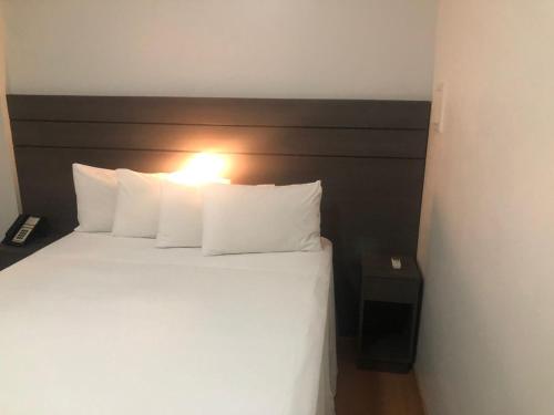uma cama com almofadas brancas e uma luz sobre ela em San Diego Apto 808 em Belo Horizonte