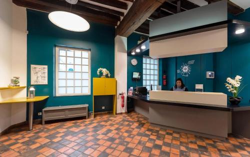 a woman sitting at a reception desk in a blue room at MIJE MARAIS Hostel in Paris