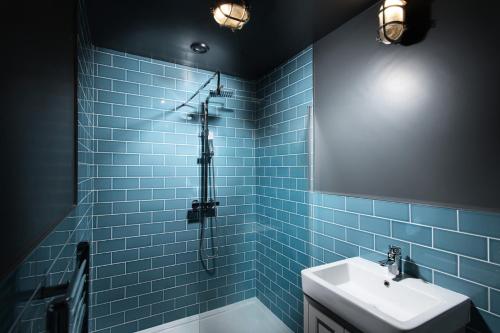 een blauw betegelde badkamer met een wastafel en een spiegel bij The Quarters in Weedon Bec