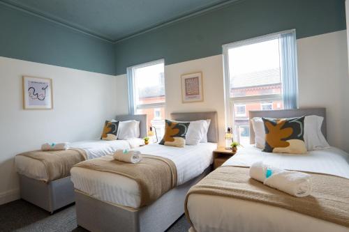 two beds in a room with two windows at Air Host and Stay - Cedar House - sleeps 7, parking, 8 mins to city in Liverpool