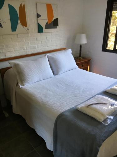 Una cama con sábanas blancas y almohadas en un dormitorio en Hermosa casa con piscina climatizada entre el mar y las sierras en Bella Vista - Piriápolis en Bella Vista