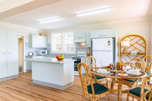 a kitchen with white cabinets and a table and chairs at Anchored at Fingal Bay 80 Marine Drive in Fingal Bay