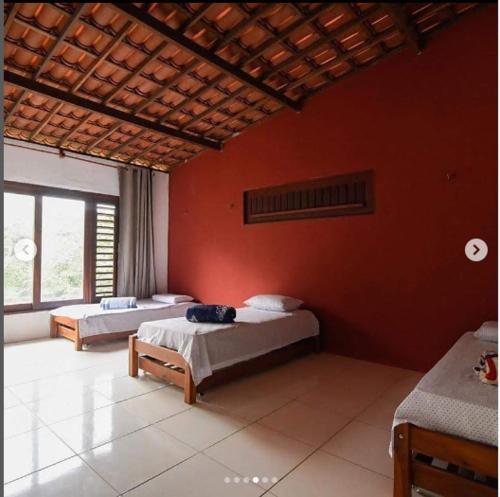 1 dormitorio con 2 camas y pared roja en Pousada Raízes Guaramiranga en Guaramiranga