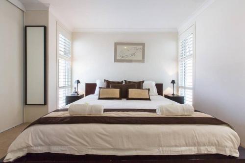 a white bedroom with a large bed with two windows at Beach View Apartment in Cottesloe in Perth