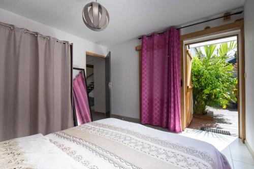 a bedroom with a bed with purple curtains and a window at LE BADAMIER in Saint-Pierre