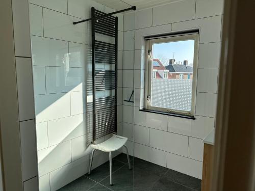 a white tiled bathroom with a chair and a window at Appartementen Beatrix in Domburg