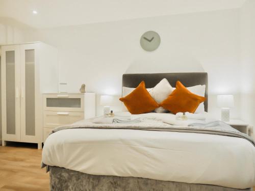 uma cama com almofadas laranja e um relógio na parede em Private Parking Stylish Great Location em Guildford