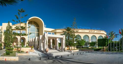 a large building with a bunch of palm trees in front of it at Carthage Thalasso Resort in Gammarth